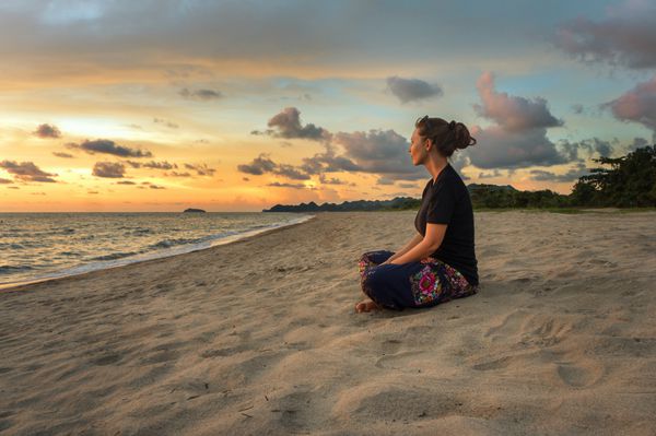 زن نشسته در شن و ماسه ساحل و آرامش در زمان غروب آفتاب