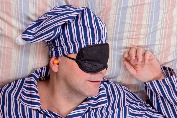 مرد با ماسک روی چشم خوابید مردی در لباس خواب راه راه خواب در رختخواب با کلاه شبانه و چشم محافظت چشم در بالا پرتره رویای مرد خوش تیپ با پچ چشم است