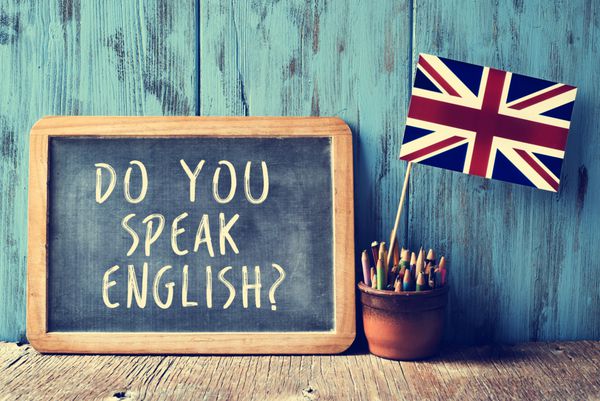 آیا شما با زبان انگلیسی صحبت می کنید؟ نوشته شده در آن یک گلدان با مداد و پرچم بریتانیا در یک میز چوبی با یک اثر فیلتر