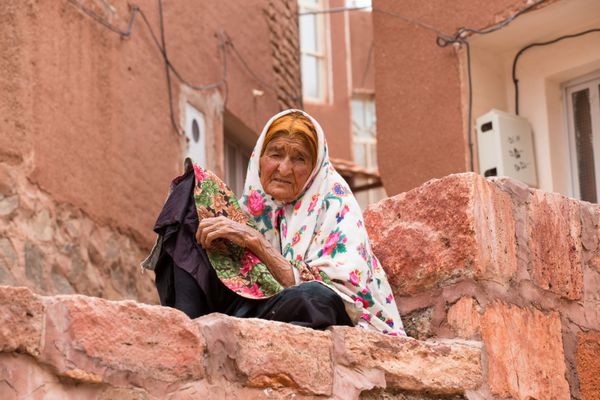 کاشان ایران 2015 مه 2 یک زن سالخورده در روستای باستانی آبیانه در نزدیکی کاشان در ایران است در پس زمینه خانه های آجری قرمز آبیانه