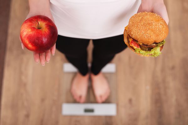 رژیم غذایی زن اندازه گیری وزن بدن در مقیاس وزن نگه داشتن دونات و سیب شیرینی ها غذاهای ناسالم هستند رژیم غذایی غذای سالم شیوه زندگی کاهش وزن چاقی نمایش بالا