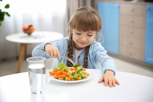 دختر کوچک خوردن سبزیجات در آشپزخانه