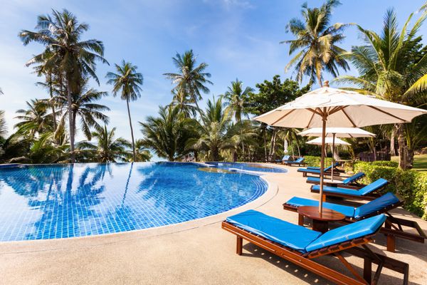 استراحت هتل با منظره ساحلی گرمسیری با استخر شنا صندلی های خورشیدی و درختان نخل در یک روز آفتابی گرم مقصد بهشت ​​برای تعطیلات