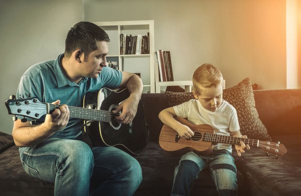 پدر پسر خود را آموزش می دهد تا در خانه گیتار بازی کند پسر بازی در Ukulele گیتار هاوایی