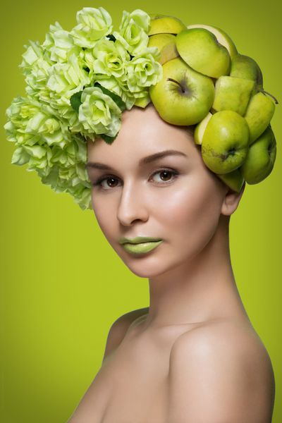تصویر انتصاب زن جوان زیبا با سیب و گل در سر بیش از پس زمینه سبز