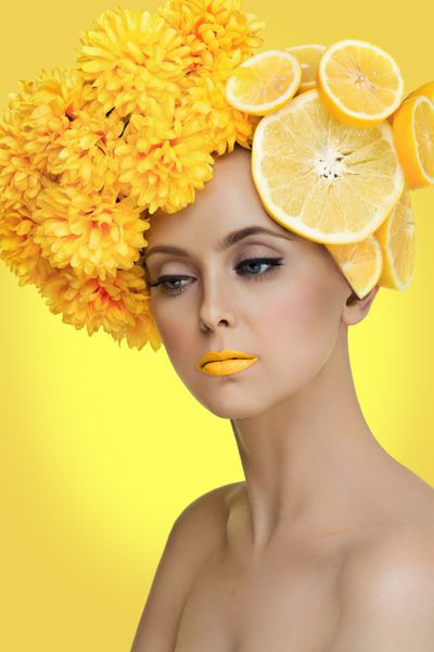 پرتره نزدیک از زن جوان زیبا با گریپ فروت لیمو و گل گل داودی در سر بیش از پس زمینه زرد
