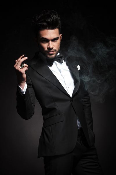 یک مرد کسب و کار خوش تیپ با استفاده از یک سیگار در حالی که یک دست در جیب خود را نگه دارید
