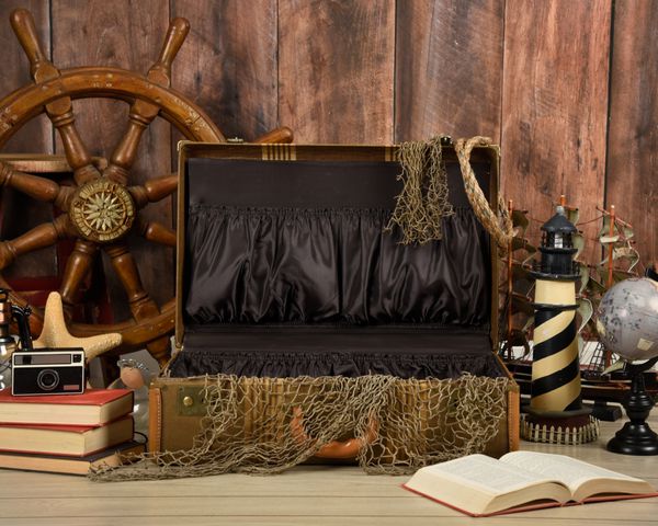 چمدان قدیم قدیمی با اشیاء مختلف اقیانوس و دریا در اطراف آن با یک دیوار چوب خالی برای یک تعطیلات یا مفهوم مسافرت باز می شود