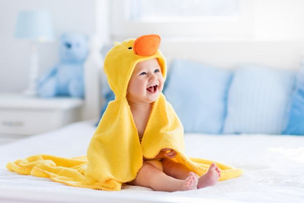 کودک خنده دار مبارک با استفاده از حوله اردک زرد با پوشش تخت نشسته روی تختخواب پدر و مادر بعد از حمام یا دوش کودک خشک را در اتاق خواب تمیز کنید حمام کردن و شستن بچه های کوچک بهداشت کودکان نساجی برای نوزادان