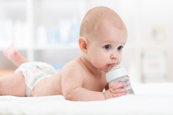 نوزاد نوشیدن آب از بطری دروغ گفتن بر روی تخت کودک پوشک را در اتاق نشیمن پوشید