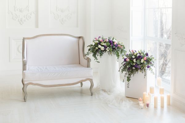 مبل سفید در اتاق و دو دسته زیبا با گل رز گل لاله و دیگر گل ها و سبز در نزدیکی آن