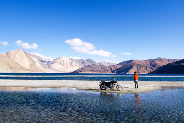 LADAKH INDIA مه 6 2016 مسافر جوان با موتورسیکلت در دریاچه Pagong در Ladakh هند دریاچه Pangong دریاچه Endorheic در Himalayas واقع در ارتفاع حدود 4350 متر است