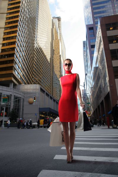 دختر جذاب در لباس قرمز با کیسه های خرید عبور از یک خیابان شهرستان