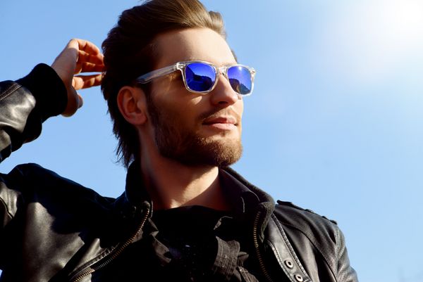 Confident handsome man in sunglasses and leather jacket over blue sky Men