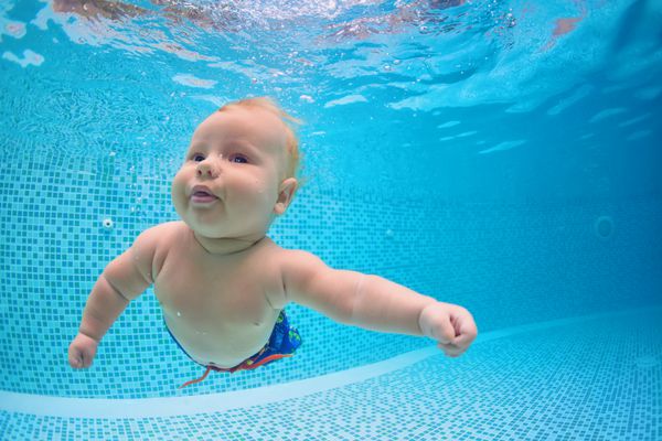 عکس خنده دار از غواصی فعال فعال در استخر شنا با لذت پرش عمیق در زیر آب کودک یاد می گیرد که شنا کند شیوه زندگی سالم کودکان تابستانی فعالیت های ورزشی آب و درس با والدین