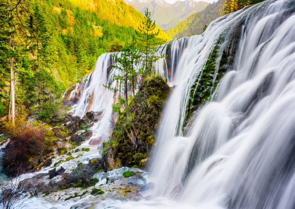 دیدگاه فوق العاده از آبشار مروارید Shoals در میان کوه های منظره ای از جنگل و جنگل های همیشه سبز در طبیعت جیوژویو پارک ملی Jiuzhai Valley چین چشم انداز پاییز شگفت انگیز در غروب آفتاب