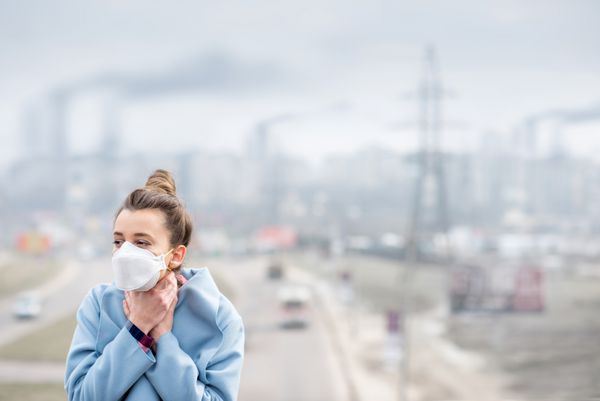 زن جوان در ماسک محافظ در شهر با آلودگی هوا از طریق ترافیک و تولید احساس بدی می کند مفهوم مفهوم