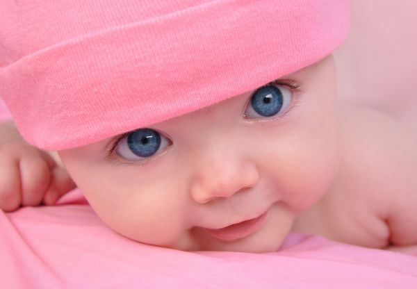 یک دختر بچه ناز کمی خیره می شود و روی پتو صورتی است او کلاه صورتی پوشانده و چشمهای آبی بزرگ دارد از آن برای یک کودک مفهوم فرزند یا عشق استفاده کنید
