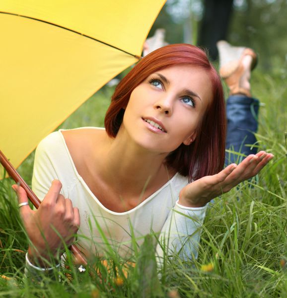 دختر زیبا آرامش بخش در چمن تحت چتر زرد