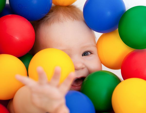 پرتره یک نوزاد خندان که در میان توپ های رنگارنگ دروغ می گوید