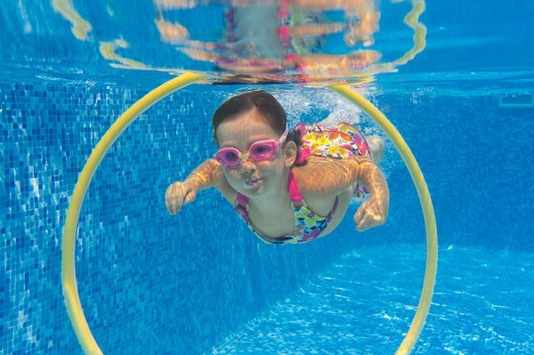 کودک مبارک در زیر زمین شنا در استخر شنا لبخند زدن دختر فعال در استخر کودکان و نوجوانان ورزش و سرگرم کننده است