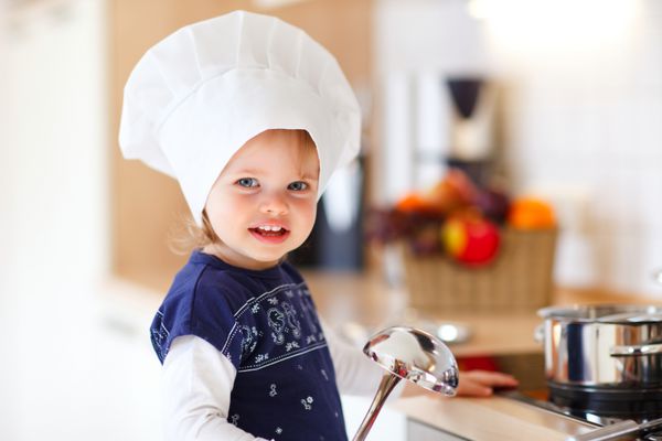 بچه کوچک دختر با کلاه سرآشپز درون آشپزخانه