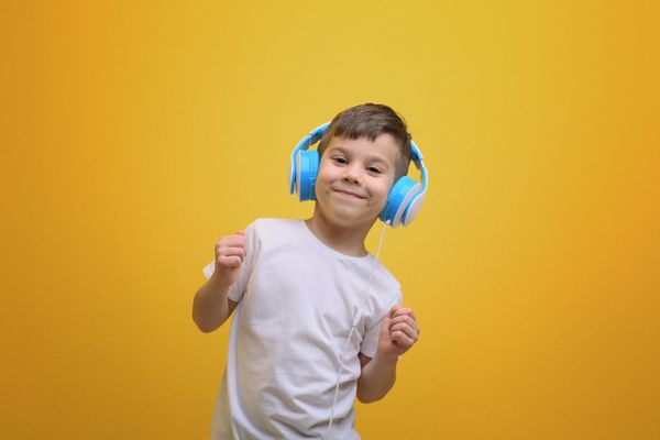 پسر کوچک ناز در هدفون گوش دادن به موسیقی در پس زمینه رنگی