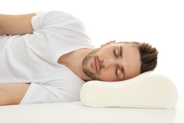 مرد جوان خوابیدن در رختخواب با بالش ارتوپدی در برابر زمینه سفید مفهوم منظر سالم