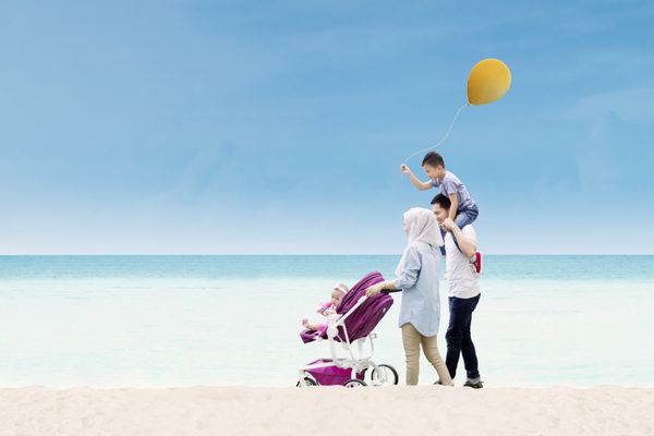 والدین جوان آسیایی وقت خود را با فرزندان خود صرف می کنند در حالی که در کنار ساحل راه می روند