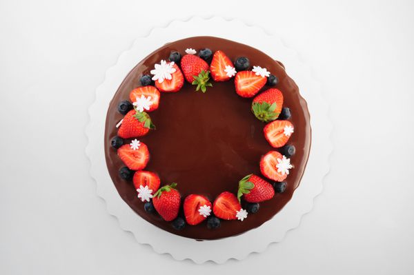 کیک تولد در شکلات با توت فرنگی زغال اخته و برف ریزه در پس زمینه سفید نمای بالا تصویر برای منو یا یک کاتولوگ شیرینی