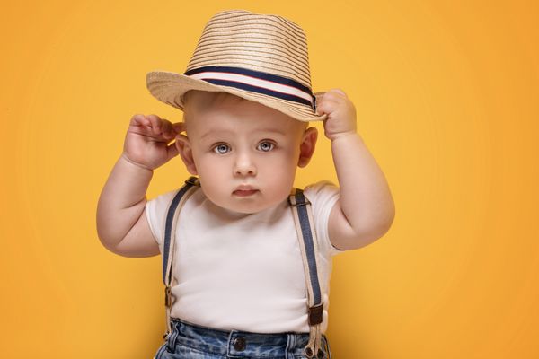 پسر بچه ناز نما در کلاه تابستان در پس زمینه زرد کودک کمی شایان ستایش در استودیو
