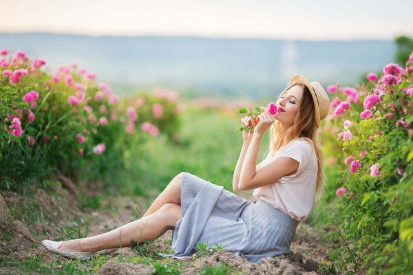 زن زیبا زیبا نشسته در گل رز در باغ مفهوم تبلیغات عطر