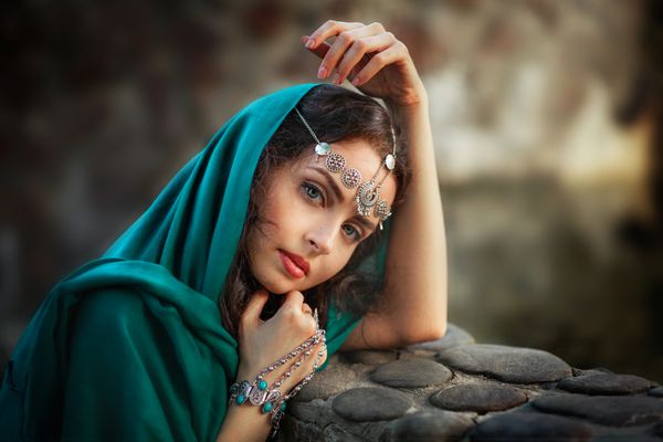 دختر زیبا در روسری و لوازم جانبی هند نشسته نزدیک دیوار سنگ و رویای زن زیبا زن به دوربین نگاه کرد