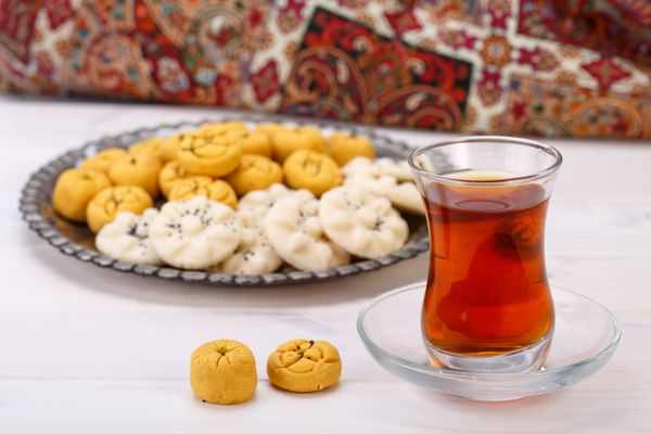 شیرینی های سنتی ایران شکلات شیرینی کیک نخود و کوکی های برنجی در صفحه توریوتیک فارسی با یک فنجان چای شیشه ای و چای سبز بر روی زمینه سفید چوبی