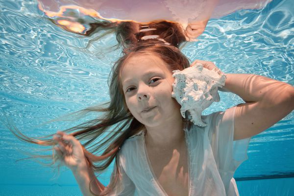 دختر کوچولو کودک در لباس سفید پرنعمت شنا در زیر آب گوش به دریای بزرگ شناور در جهان فوق العاده زیبا زیر آب جهان مدل موی فانتزی و پری