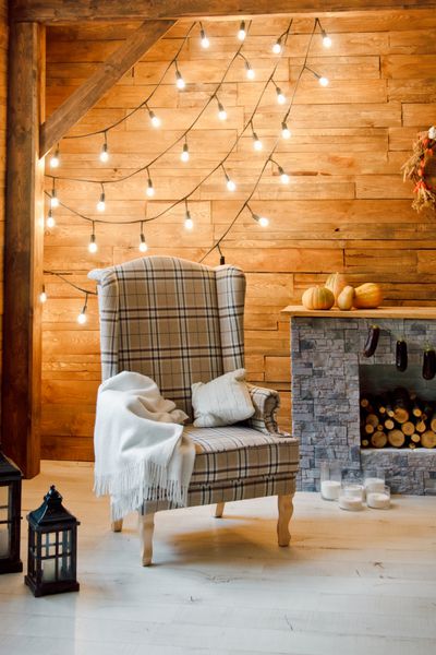 راحتی خانه صندلی در کنار شومینه با هیزم عکس داخلی اتاق با دیوار چوبی جاروها و جواهرات فضای کریسمس