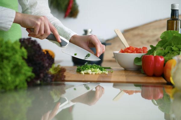 نزدیک از دست انسان پخت و پز سبزیجات سالاد در آشپزخانه بر روی میز شیشه ای با انعکاس