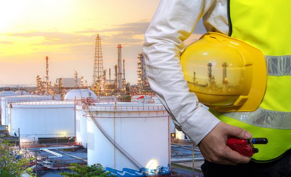مهندسانی که کلاه ایمنی زرد را در دست نگه دارند و نگهداری قرمز در دست با مخازن نفت مخزن نفت پس زمینه پالایش نفت و گاز با گرگ و میش