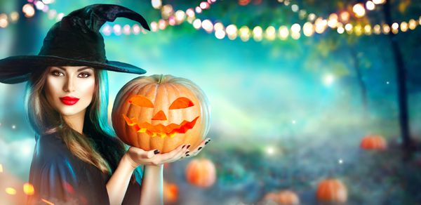 جادوگر هالووین با کدو تنبل و چراغ سحر و جادو در یک جنگل تاریک زن زیبا زن شگفت زده در جادوگران کلاه و صحنه و لباس کدو تنبل طراحی هنری حزب هالووین