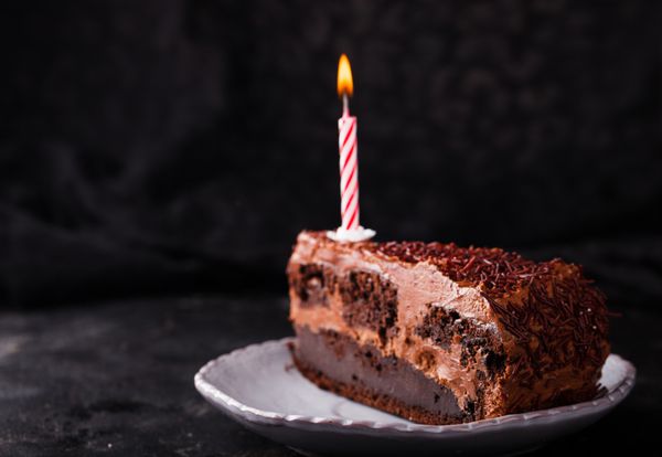 قطعه شکلات کیک با شمع در پس زمینه تاریک