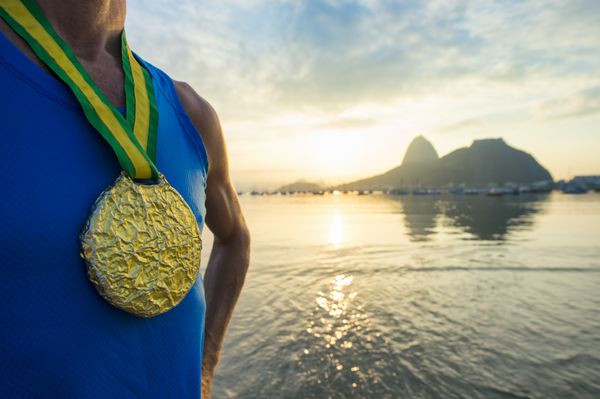 مدال طلای ورزشکار قهرمان ایستاده در خارج از منزل در طلوع آفتاب طلایی مقابل کوه کله قند در ریودوژانیرو برزیل