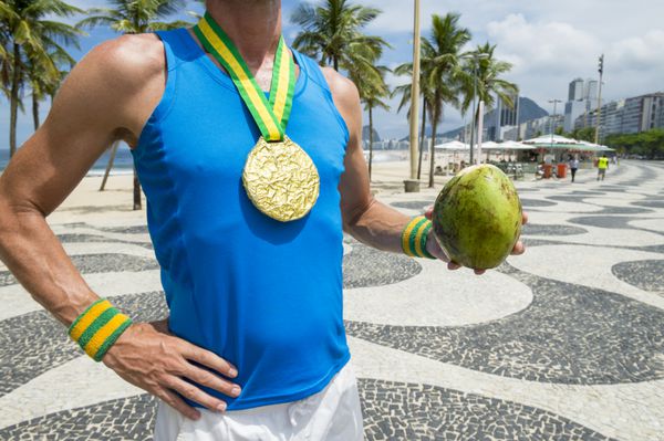 مدال طلای ورزشکار ایستاده با نارگیل سبز کوک ژله ای در سقف کاذب در Copacabana Beach ریودوژانیرو برزیل