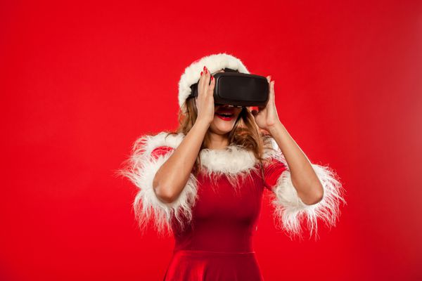 کریسمس X-mas زمستان مفهوم شادی سبیل زیبا جوان با موهای بلند در Santa کلاه زنانه پوشیدن رئوس مطالب واقعیت مجازی در پس زمینه قرمز