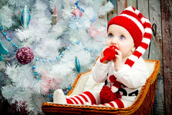 لبخند زدن دختر بچه نشسته در زیر درخت آبی در یک کلاه راه راه قرمز و سفید رنگ است مفهوم یک سال جدید در یک کارت کریسمس