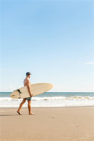 مرد با تخته موج سواری در کنار ساحل دریا در تابستان