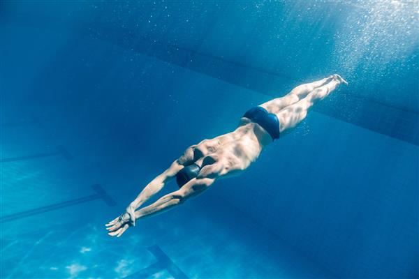 تصویر شناگر در حال شنا در استخر از زیر آب