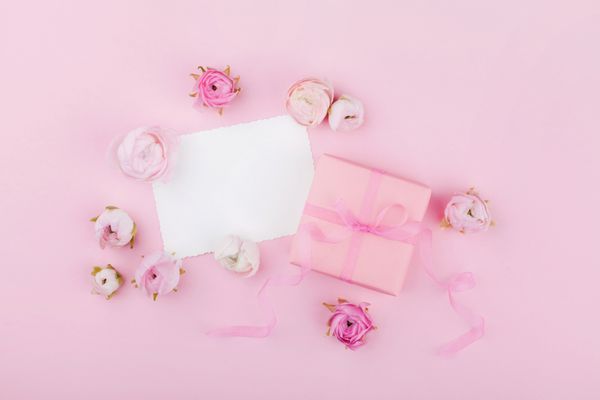 هدیه یا جعبه حاضر گل کاغذ سفید و گل بهار روی میز صورتی از بالا برای طراحی عروسی و یا کارت تبریک در روز زنان در سبک نازک صاف