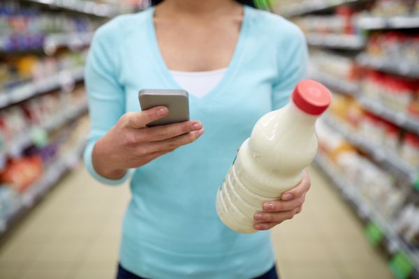 زن با گوشی هوشمند خرید شیر در سوپرمارکت