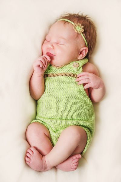 دختر نوزاد تازه متولد شده در جوراب شلواری سبز و دکوراسیون گل کوچک روی سر است