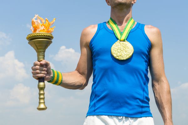 ورزشکار مدال طلای برزیل با مشعل ورزش در مقابل آسمان آبی در ریودوژانیرو برزیل ایستاده است
